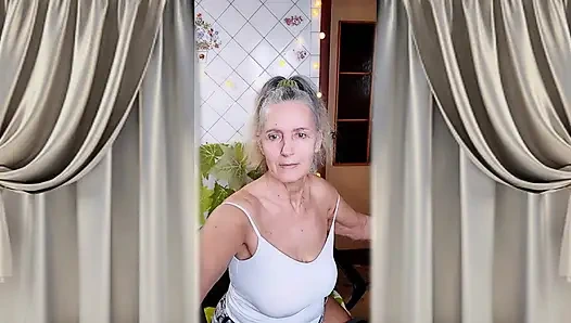 A cheerful housewife twerks in the kitchen near the washing machine and beckons with her bare feet.