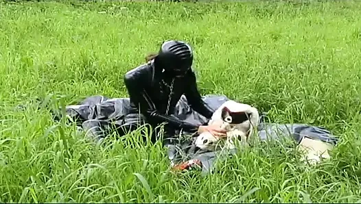 Fetish slave in latex walks and sucks a dildo on the grass