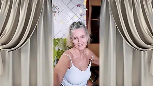 A cheerful housewife twerks in the kitchen near the washing machine and beckons with her bare feet.