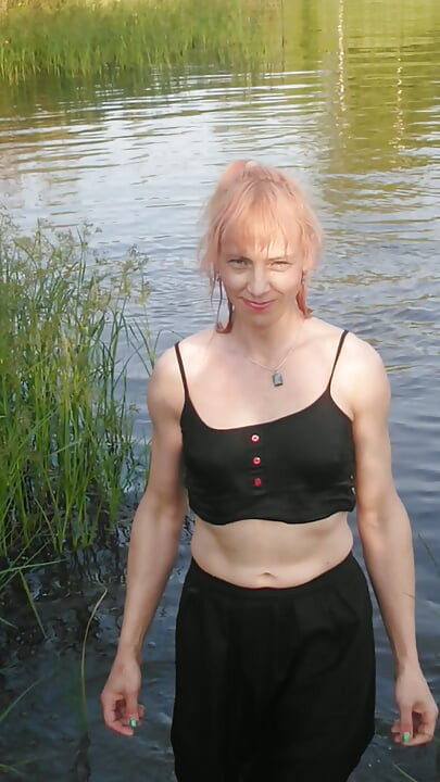 Trans kız gölde kıyafetleriyle yüzerken tamamen siyah giyiniyor: külotlu çorap, etek ve üst. Wetlook gölde.
