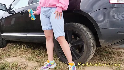 Hipster girl with a hoodie pee trough her jeans and pee next to the wheel of the car