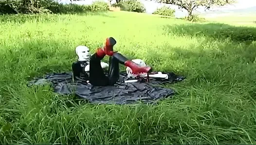 Lateksli fetiş köle yürüyor ve çimlerde dildo emiyor