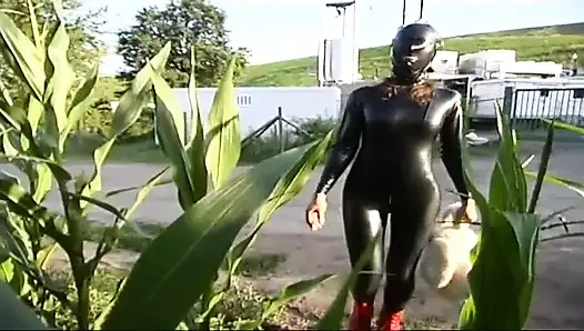 Lateksli fetiş köle yürüyor ve çimlerde dildo emiyor