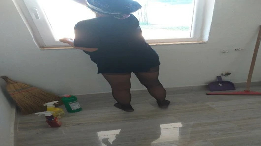 Başörtülü olgun kadın evin camını siliyor.